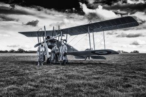 Black and white photo of WWI-era re-enactors standing beside a period biplane