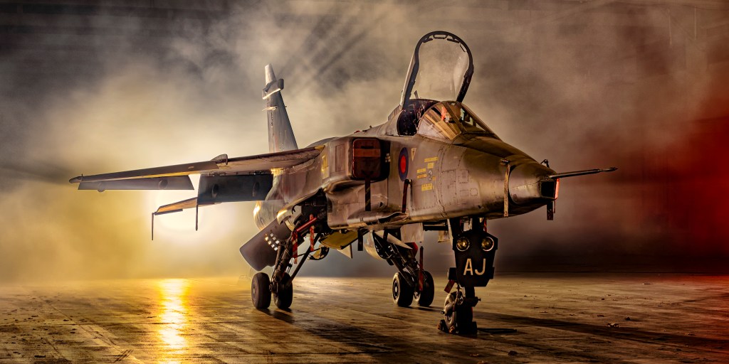 SEPECAT Jaguar fighter jet dramatically lit with smoke and golden light in a hangar