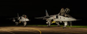 Two SEPECAT Jaguar aircraft floodlit at night on an airfield apron