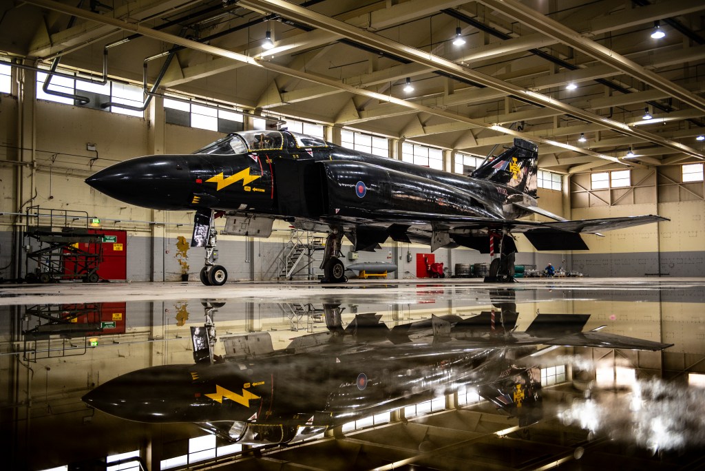 Black-liveried McDonnell Douglas F-4 Phantom fighter jet reflected on a polished hangar floor