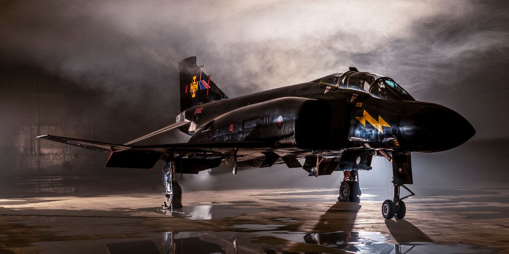 Black-liveried F-4 Phantom fighter jet shrouded in atmospheric smoke inside a hangar