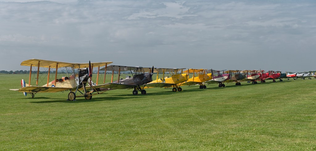 Line-up of vintage biplanes including Tiger Moths and an RE8 on the grass at Duxford
