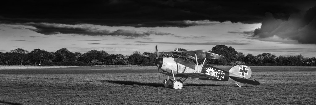 Black and white view of an Albatros D.Va replica parked on grass beneath heavy cloud with German crosses on its fuselage and tail