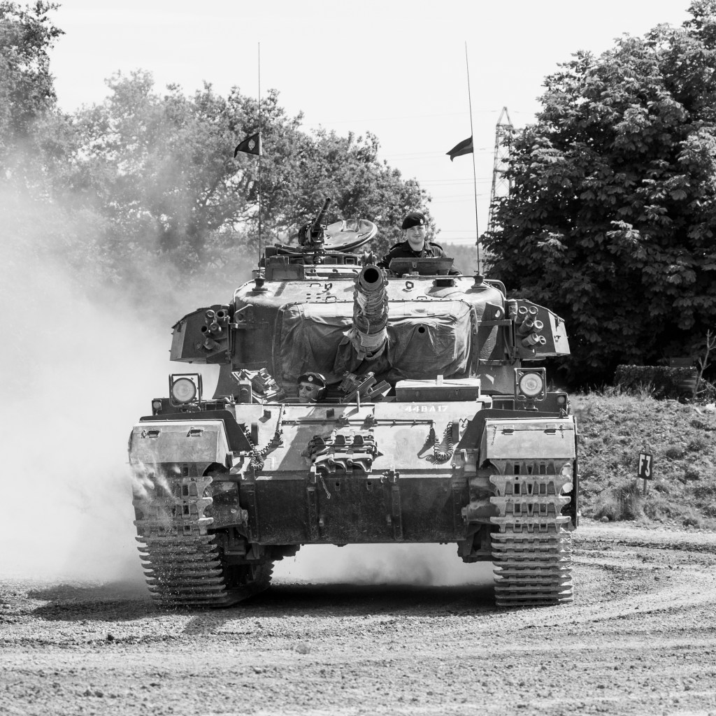 Black and white front view of Centurion 44BA17 driving through dust with its commander in the turret