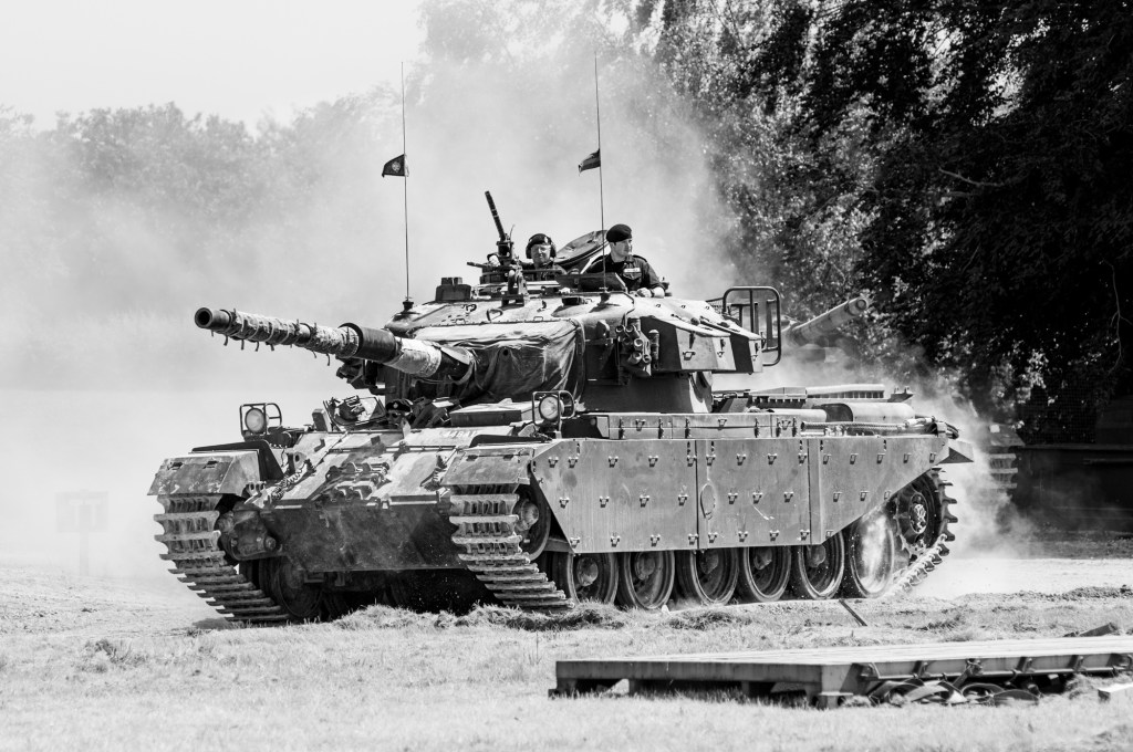 Black and white side view of Centurion 44BA17 moving through dust with two crew in the turret