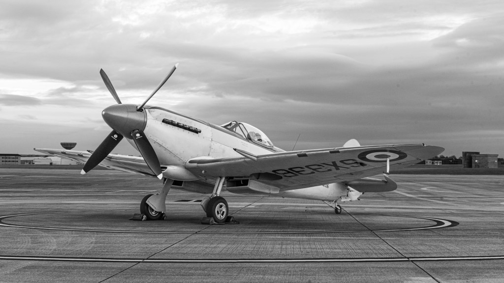 Black and white three-quarter view of Seafire SX336 on the apron under a cloudy evening sky
