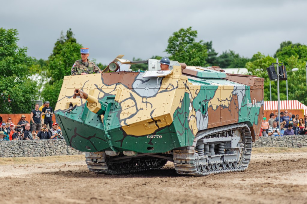French Saint-Chamond tank in green, tan and brown camouflage driving across the arena at Tankfest, Bovington, with spectators behind