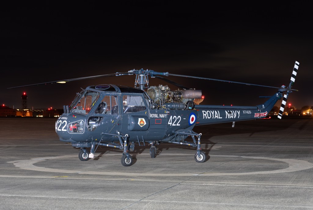 Westland Wasp XT420, number 422, in Royal Navy markings on the apron at RNAS Yeovilton at night with airfield lights behind.